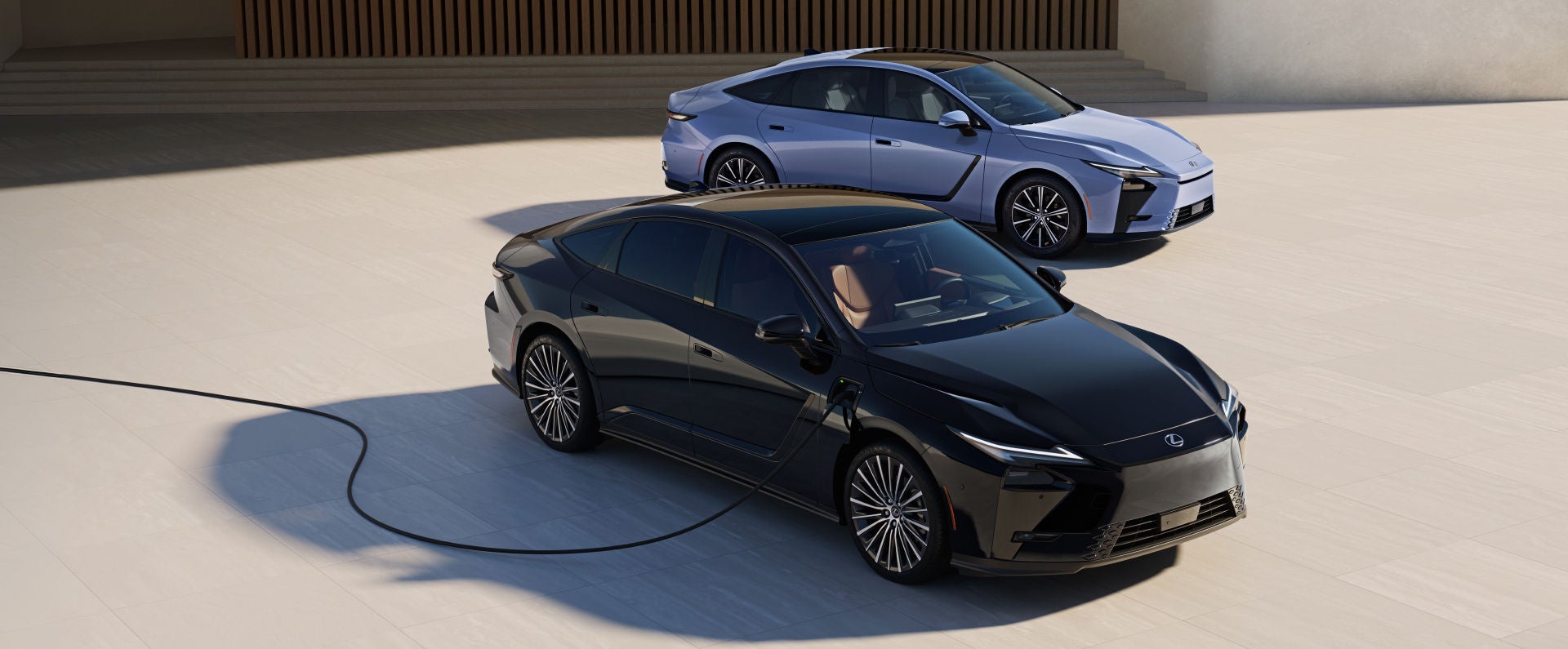 Lexus ES Hybrid shown in Wavelength exterior color, alongside a Lexus ES 500e shown in Caviar exterior color, which is connected to a home charging station.