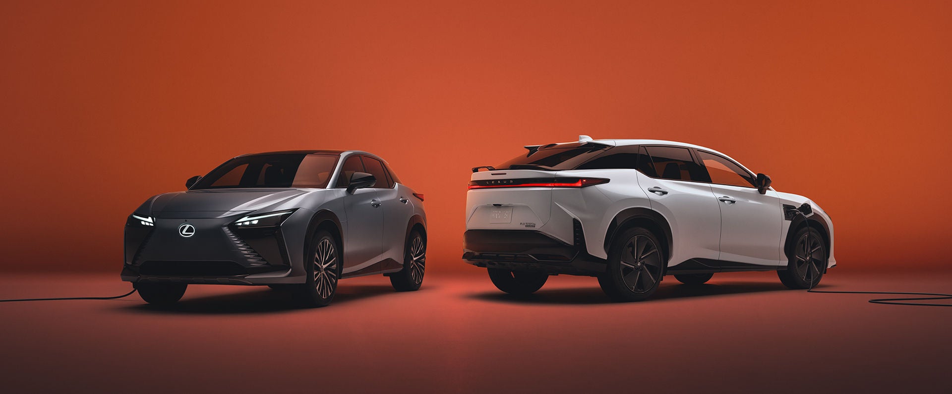 Two Lexus RZ vehicles, in Cloudburst Gray on left and Oxygen White on right, shown with charging cables.