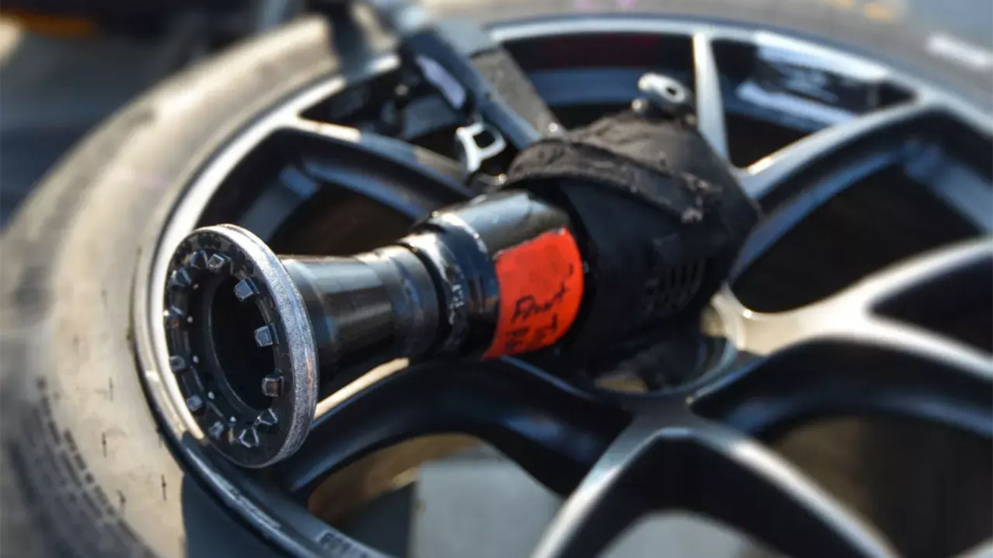 Close-up of a racing wheel nut socket tool with an orange label resting on a black alloy wheel rim.
